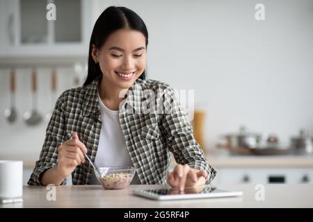 Young asian woman having breakfast and using digital tablet Stock Photo