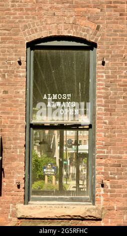 Window on a red brick building with the sign saying in white lettering, Almost Always Open. Stock Photo