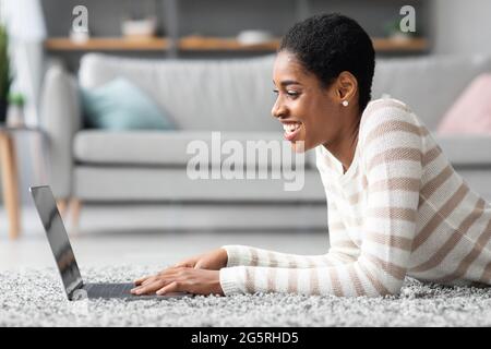 Side View Of Cheerful Black Woman Using Laptop Computer At Home Stock Photo