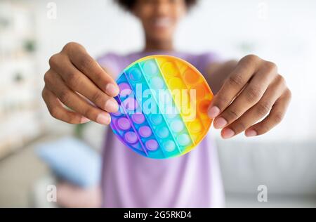 Cropped view of black teenager holding POP IT toy in outstretched hands at home, closeup Stock Photo