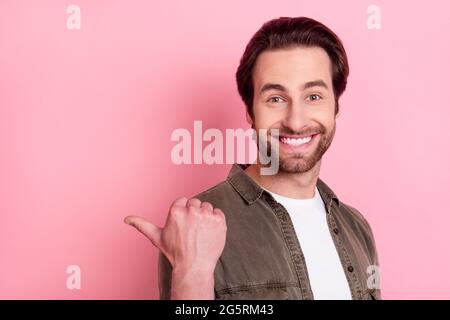 Photo of impressed pretty young guy dressed brown shirt pointing thumb empty space isolated pink color background Stock Photo