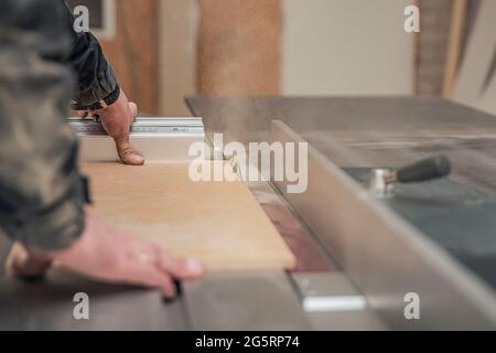 A carpenter works on a woodworking machine. Saws furniture pieces with a circular saw. The process of sawing parts piece by piece Stock Photo