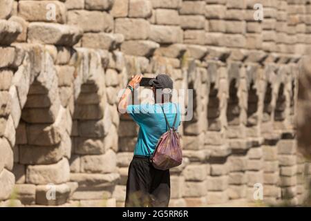 Segovia, Spain - June 2, 2021: An older adult man, probably a foreign tourist, takes pictures of the granite columns of the Aqueduct of Segovia Stock Photo