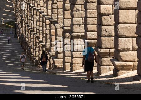 Segovia, Spain - June 2, 2021: Detail of the huge granite columns of the Aqueduct of Segovia, and some people, from Teodosio el Grande street Stock Photo
