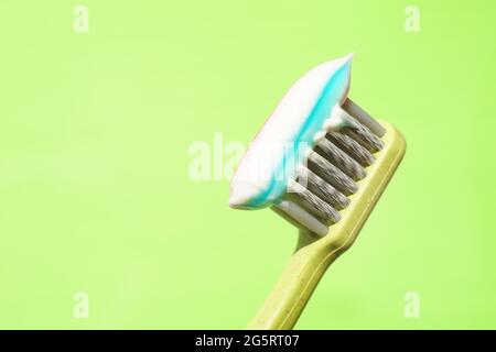 Green plastic toothbrush with striped toothpaste on green background. Stock Photo