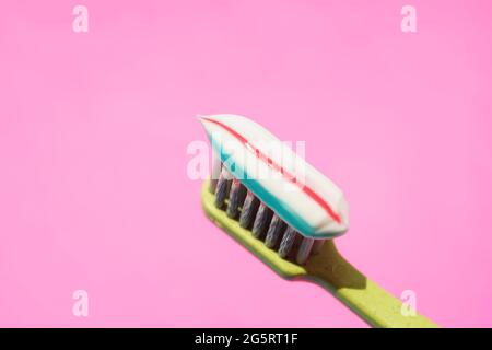 Green plastic toothbrush with striped toothpaste on pink background. Stock Photo