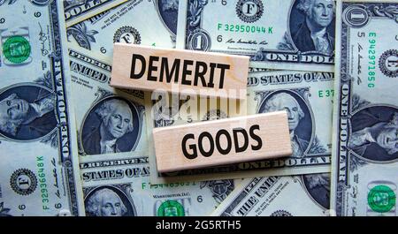 Demerit goods symbol. Wooden blocks with words Demerit goods on beautiful background from dollar bills, copy space. Business and demerit goods concept Stock Photo