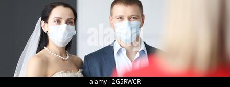 Bride and groom wearing medical protective masks standing in front of receptionist Stock Photo