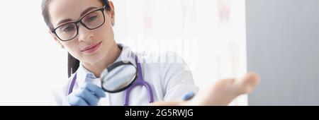 Woman podiatrist examining heel of patient using magnifying glass Stock Photo