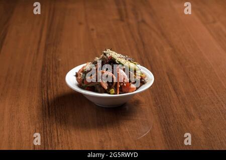 Korean salad with eggplant, cucumbers, tomatoes, carrots and sesame seeds in a white plate on the table Stock Photo