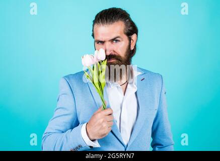 smelling good. brutal handsome man with gift. valentines or womens day. masculinity and charisma. formal party dress code. bearded hipster hold tulip Stock Photo