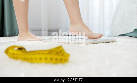 Female feet walking and standing on weights in bedroom. Concept of dieting, loosing weight and healthy lifestyle. Stock Photo