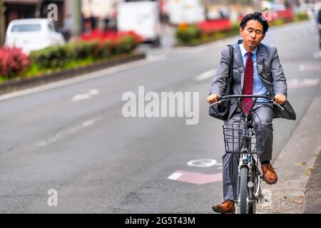 Kyoto, Japan - April 17, 2019: Japanese person on bicycle riding bike on street road candid city life in traffic near station with business suit and b Stock Photo