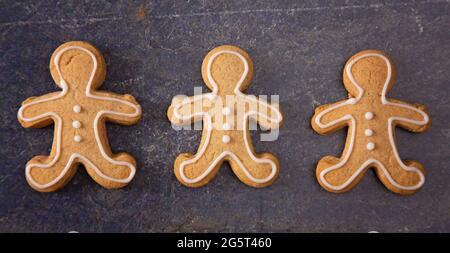 A Line of Three Decorated Gingerbread Men on a Dark Surface Stock Photo
