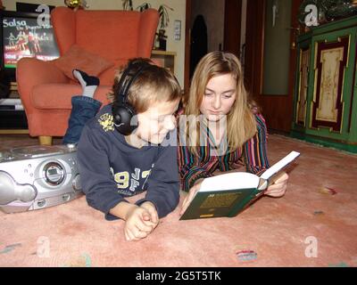 brother and sister lie on the floor together and looking into a book Stock Photo