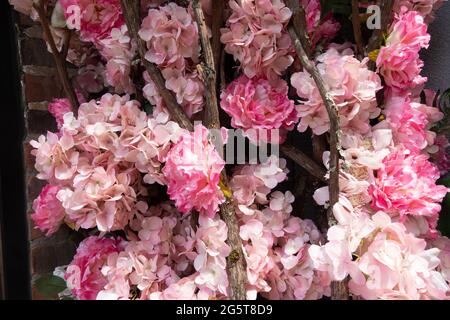 Close-up of a decorative floral arrangement with pink and light pink artificial hydrangeas and wooden sticks against a brick wall Stock Photo