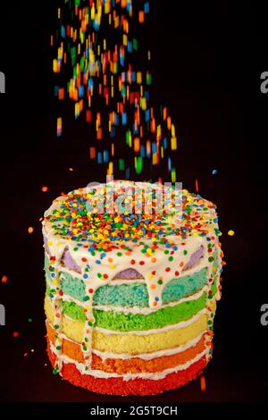 Sprinkling with sugar sprinkles on homemade rainbow cake with white cream. Stock Photo