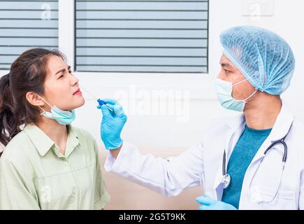 Coronavirus test, Doctor man take saliva sample through nose with cotton swab to check coronavirus test from Asian young woman, Covid-19 pandemic outb Stock Photo