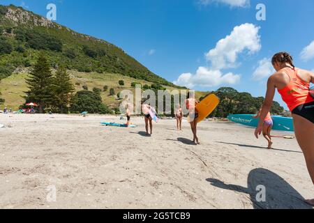 Mount maunganui New Zealand -January 20 2015; Teenagers carrying paddle boards along beach as one entering frame following shadow. Stock Photo