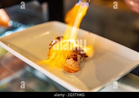 Close up hand of chef using kitchen torch burn on salmon sushi, japanese cuisine. Stock Photo