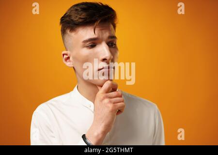 Portrait of thoughtful young man who looks away touching his chin Stock Photo