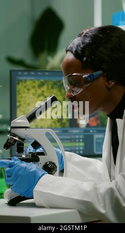 Biologist woman looking at test sample under microscope working at gmo experiment. Pharmaceutical scientist analyzing organic agriculture plants in microbiology scientific laboratory Stock Photo