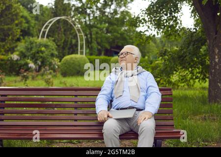 Happy senior man with a laptop computer sitting on a bench in a green summer park Stock Photo