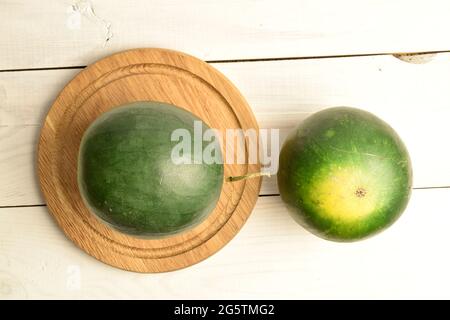 Two ripe organic watermelons with a round wooden tray, close-up, on a white wooden table, top view. Stock Photo