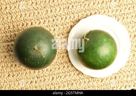 Two ripe organic watermelons with a white saucer, close-up, on a straw mat, top view. Stock Photo