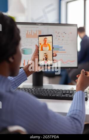 Handicapped invalid african manager talking on videocall with friends holding mobile working at financial project of company , taking break during work time. Employee sitting immobilized in wheelchair. Stock Photo