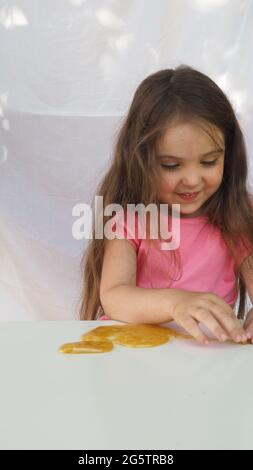 Kid Playing Hand Made Toy Called Slime. cute girl in a pink t-shirt plays with a yellow slime. contemporary creativity. stretching, scamming, modeling Stock Photo