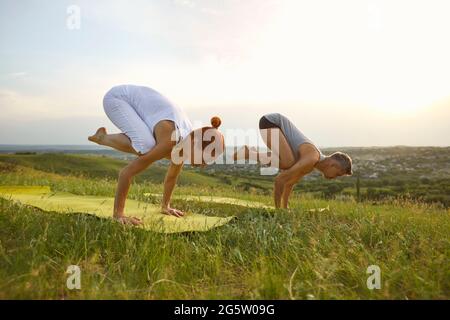 Couple doing bakasana position and practicing yoga together on nature outdoors Stock Photo