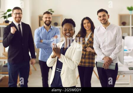 Happy business leader clapping hands standing in office with team of her employees Stock Photo