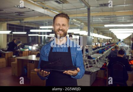 Smiling shoe factory worker standing in the workshop and showing a new leather boot Stock Photo