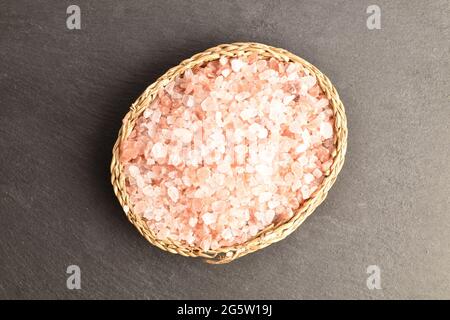 Rock salt of pink color in a straw salt shaker, close-up, on a slate board, top view. Stock Photo