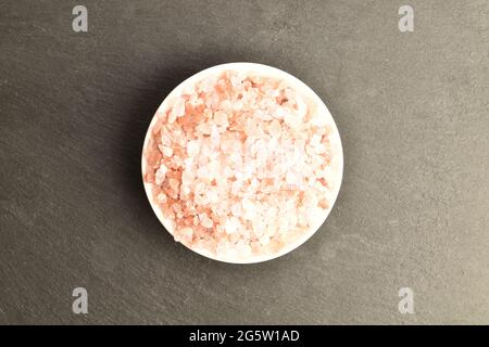 Pink rock salt in a ceramic salt shaker, close-up, on a slate serving board, top view. Stock Photo