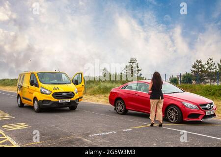 Lady driver alone Southport, Merseyside.  Uk Weather 30 June 2021,   Early morning 24hr roadside assistance from AA yellow recovery van as motorist suffers a puncture on the coastal road. Stock Photo