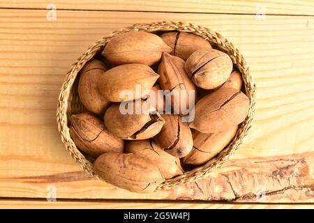 Several organic ripe pecans in a straw plate, close-up, on a wooden table, top view. Stock Photo