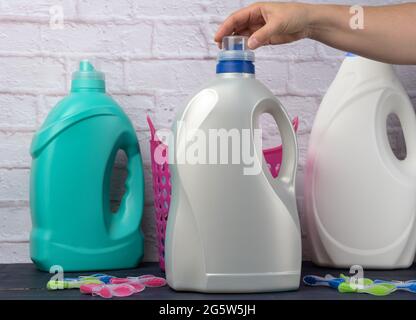 woman's hand holding a large white plastic bottle with detergent for washing clothes against a white brick wall background Stock Photo