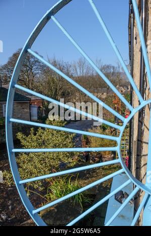 An unusual iron wheel protecting the walkway over the bridge at Hayfield, Derbyshire with cottages and countryside beyond. Stock Photo
