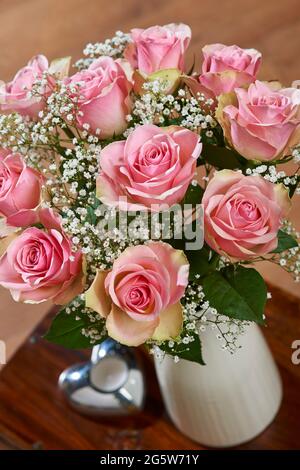 Mixed bouquet of soft pink roses and gypsophila in a vase on a coffee table in a home setting Stock Photo