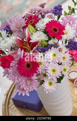A large mixed bouquet of flowers in a vase on a small coffee table in a room setting Stock Photo