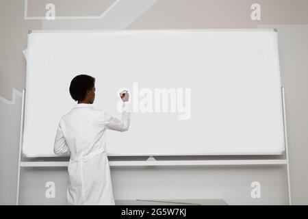 African American black woman math teacher writing on empty white board with marker rear view. Stock Photo