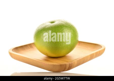 One organic bright green Citrus Sweetie on a bamboo plate, close-up, isolated on white. Stock Photo