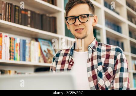 Young smiling student taking notes on textbook preparing for exam, man doing homework sitting at work table with modern laptop computer Stock Photo