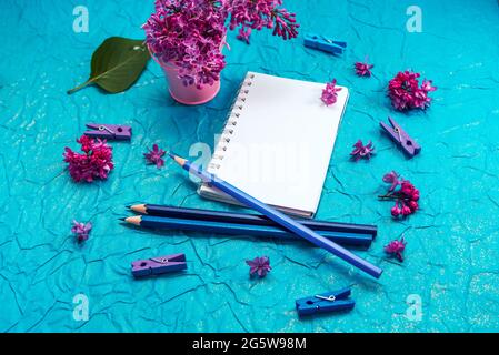 Blank notebook, pencils and lilac flowers on vintage painted blue cardboard background Stock Photo
