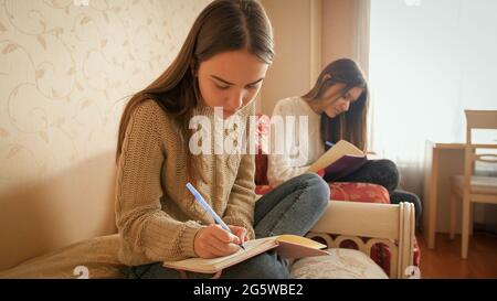 Two teenage sister doing homework and writing in copybooks. Teens studying Stock Photo