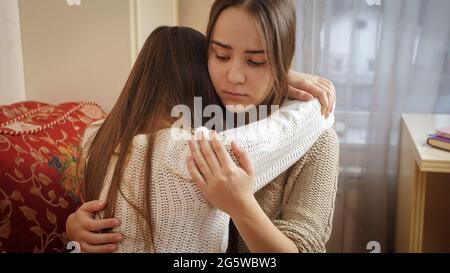 Teenage girl hugging and consoling her crying friend at bedroom. Friends support and teenager depression Stock Photo