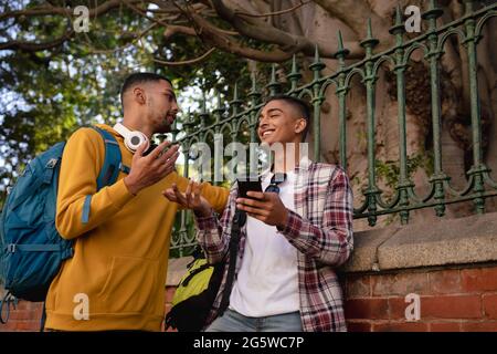 Two smiling mixed race male friends with backpacks standing in street talking Stock Photo