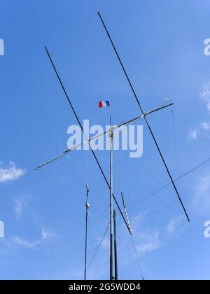 Amateur radio antenna surmounted by a French flag flying in the wind on a deep blue sky. Stock Photo